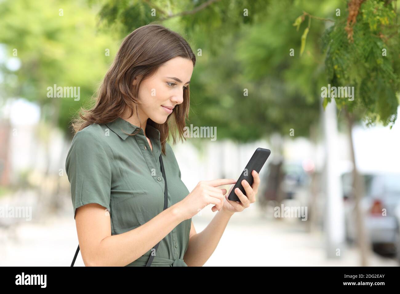 Vista laterale ritratto di una donna seria che cammina con Smart telefono in strada Foto Stock