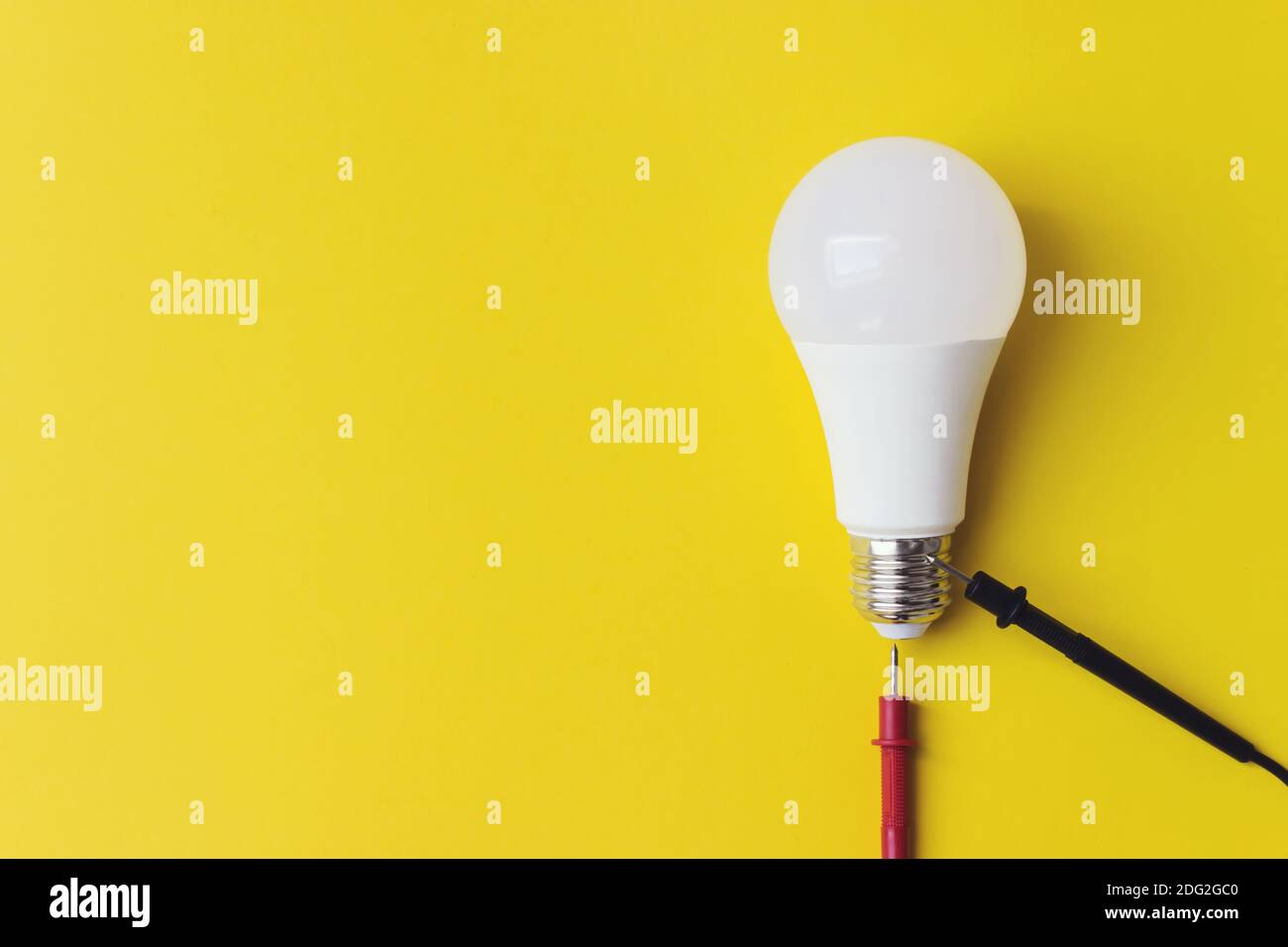 Lampadina incandescente con sonde del multimetro su sfondo giallo, concetto di unicità. Idea, innovazione, concetto di creatività, Foto Stock