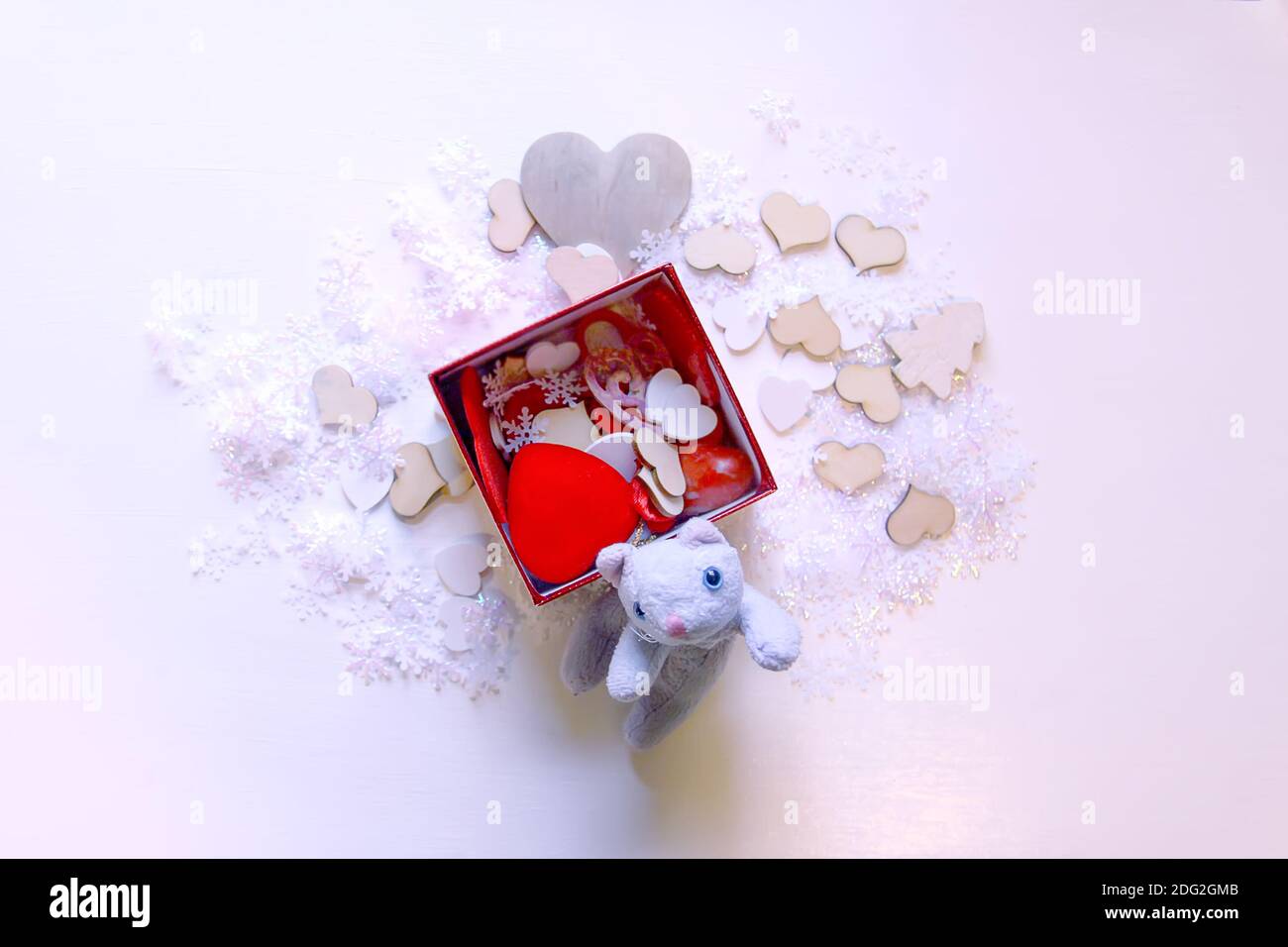 Fiocchi di neve artificiali, gattino giocattolo e cuori decorativi rossi su sfondo bianco morbido. Capodanno e Natale decorazione. Foto Stock