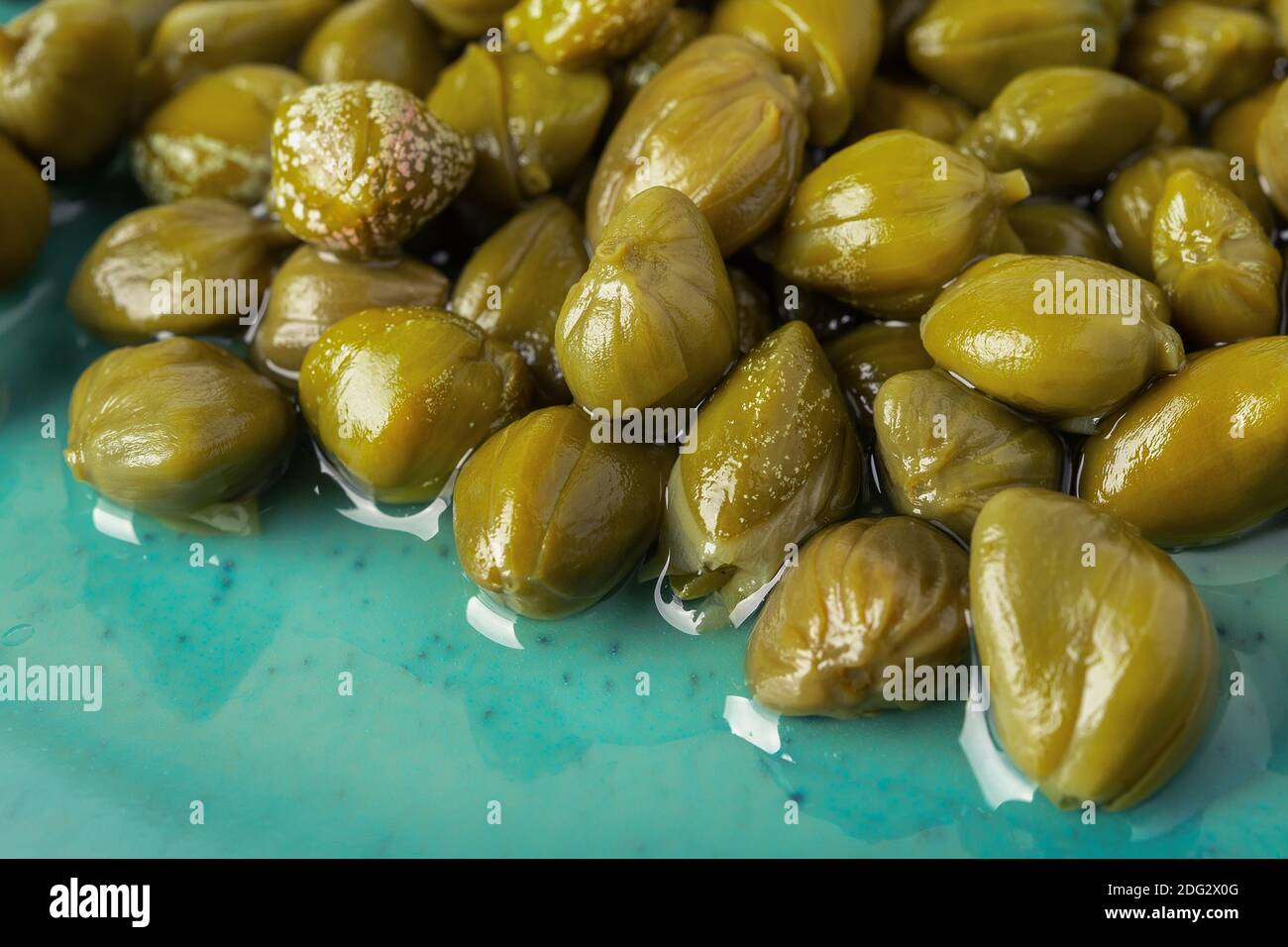 Primo piano di capperi decapati su un piatto turchese. Gemme marinate di cappero cespuglio. Ingredienti della cucina mediterranea. Spezie e condimenti biologici. Foto Stock