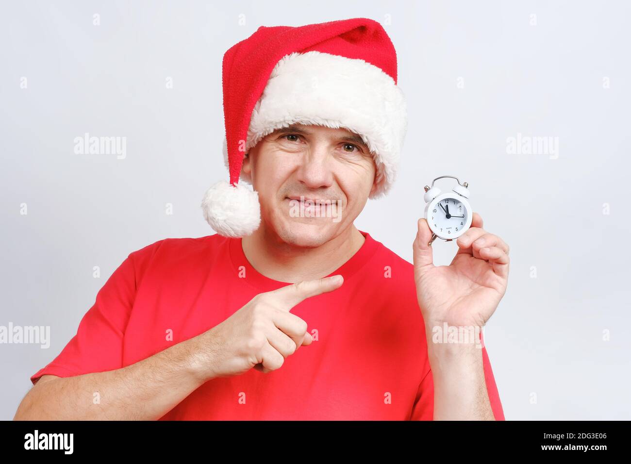 Sorridente caucasico di mezza età in Santa cappello mostrando con il dito a. sveglia Foto Stock