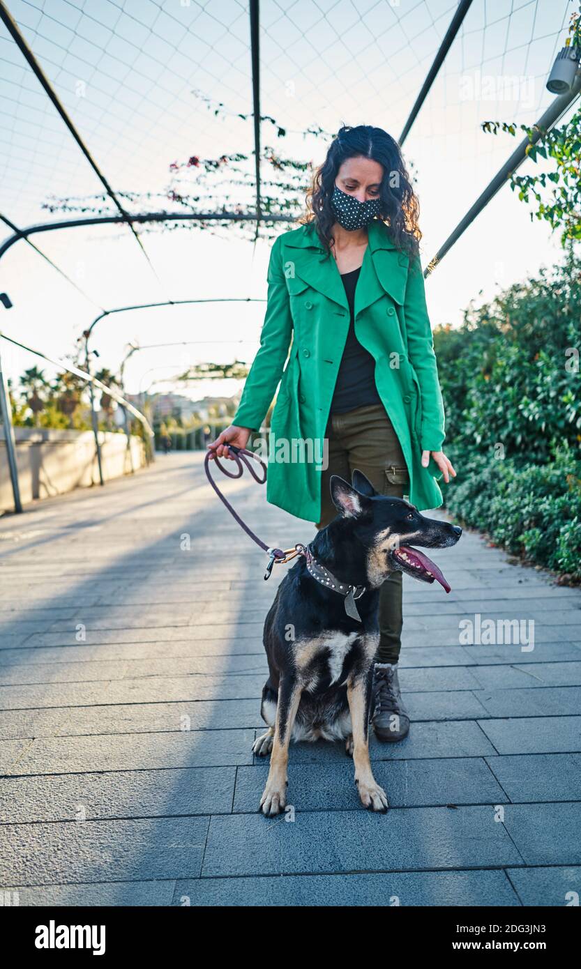 Un colpo verticale di una giovane donna che indossa un cappotto verde camminando il suo cane nel parco Foto Stock
