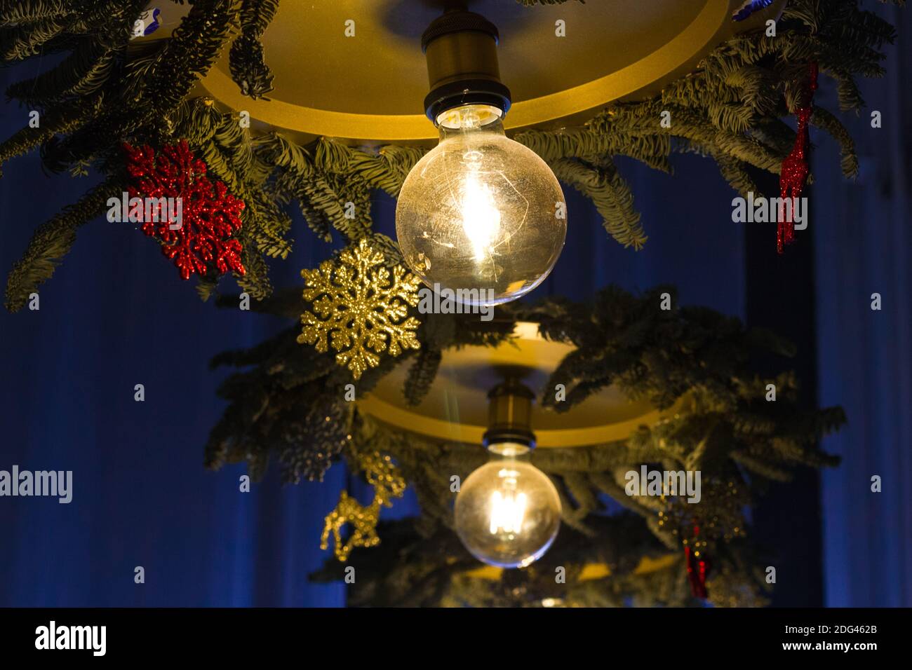 Lampadario con lampade illuminate decorate stagionalmente per Natale con fiocchi di neve gialli e rossi e rami di pino su un blu sfondo Foto Stock