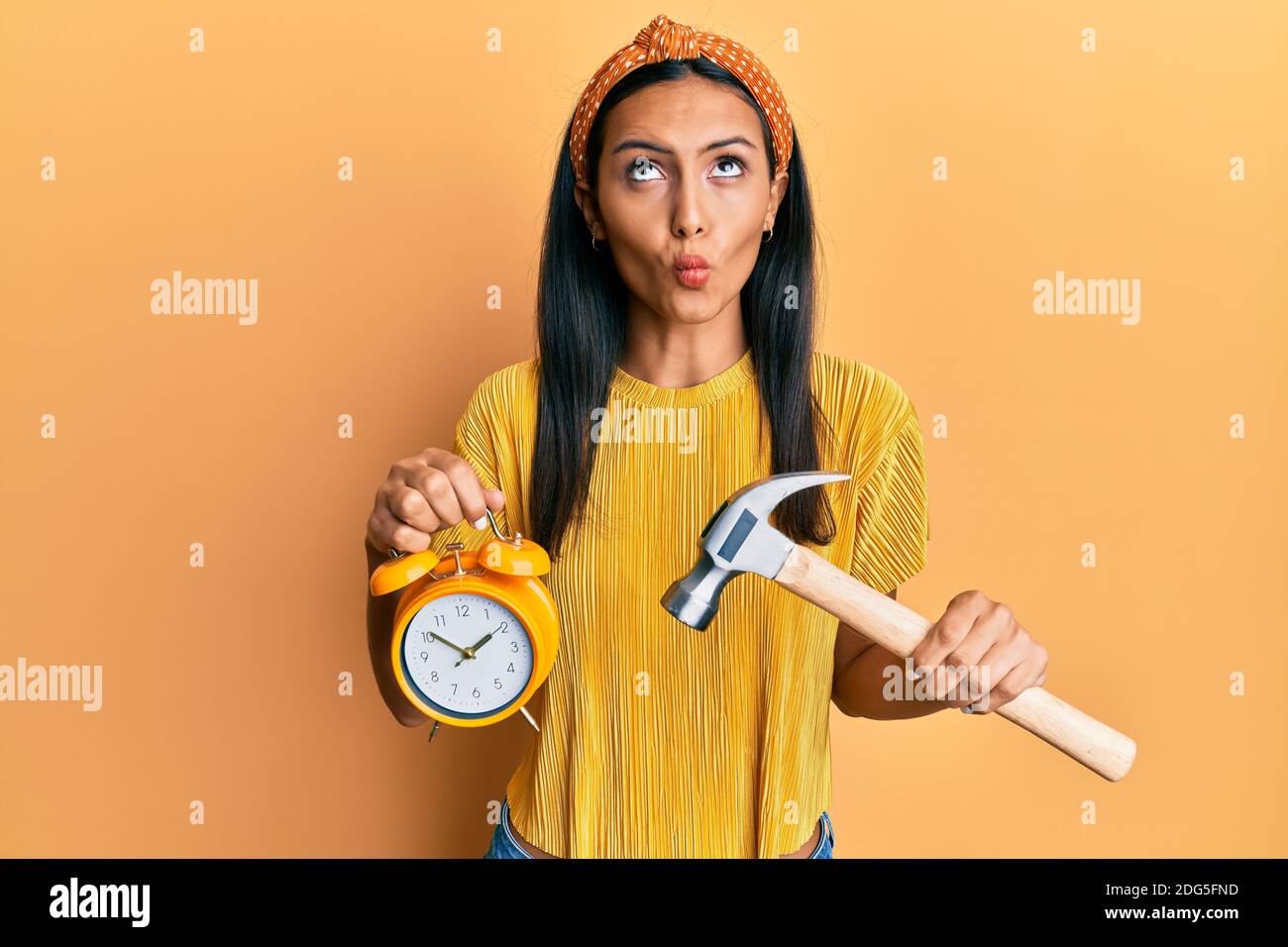 Giovane donna bruna che tiene sveglia e martello che fa faccia di pesce con  bocca e occhi squinting, pazzo e comico Foto stock - Alamy