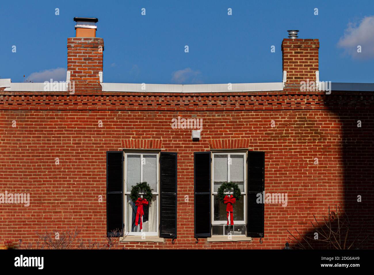 Un edificio in mattoni d'epoca con decorazioni per finestre caratterizzato da corone natalizie di pino con nastri rossi. La vecchia casa ha due camini in cima. Cielo limpido Foto Stock