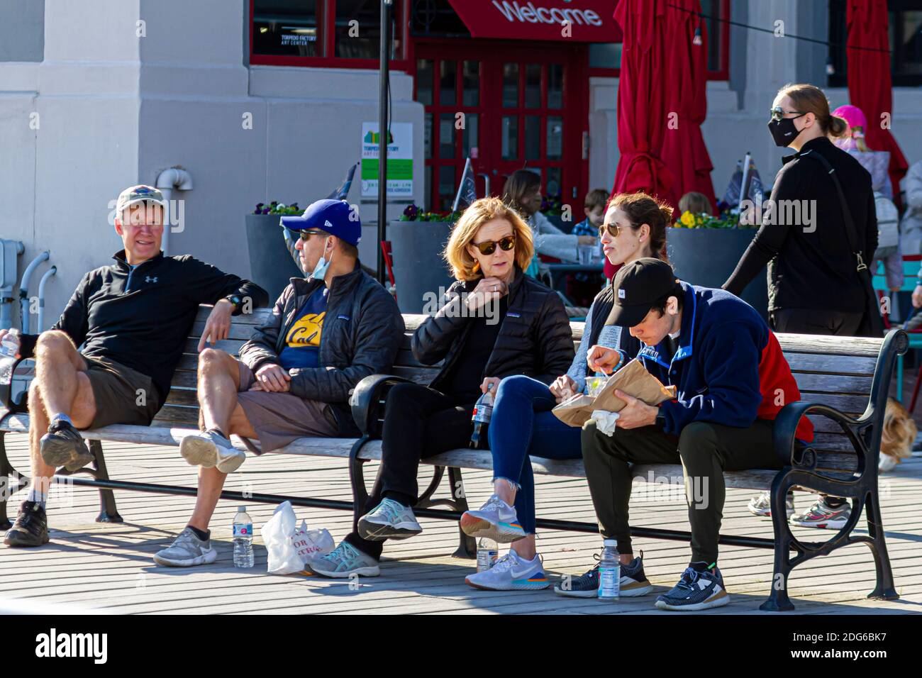 Alexandria, VA, USA 11-28-2020: Un gruppo di persone sono in panchina in un luogo affollato che snacking su nibbles. Non indossano maschere facciali o a distanza sociale Foto Stock
