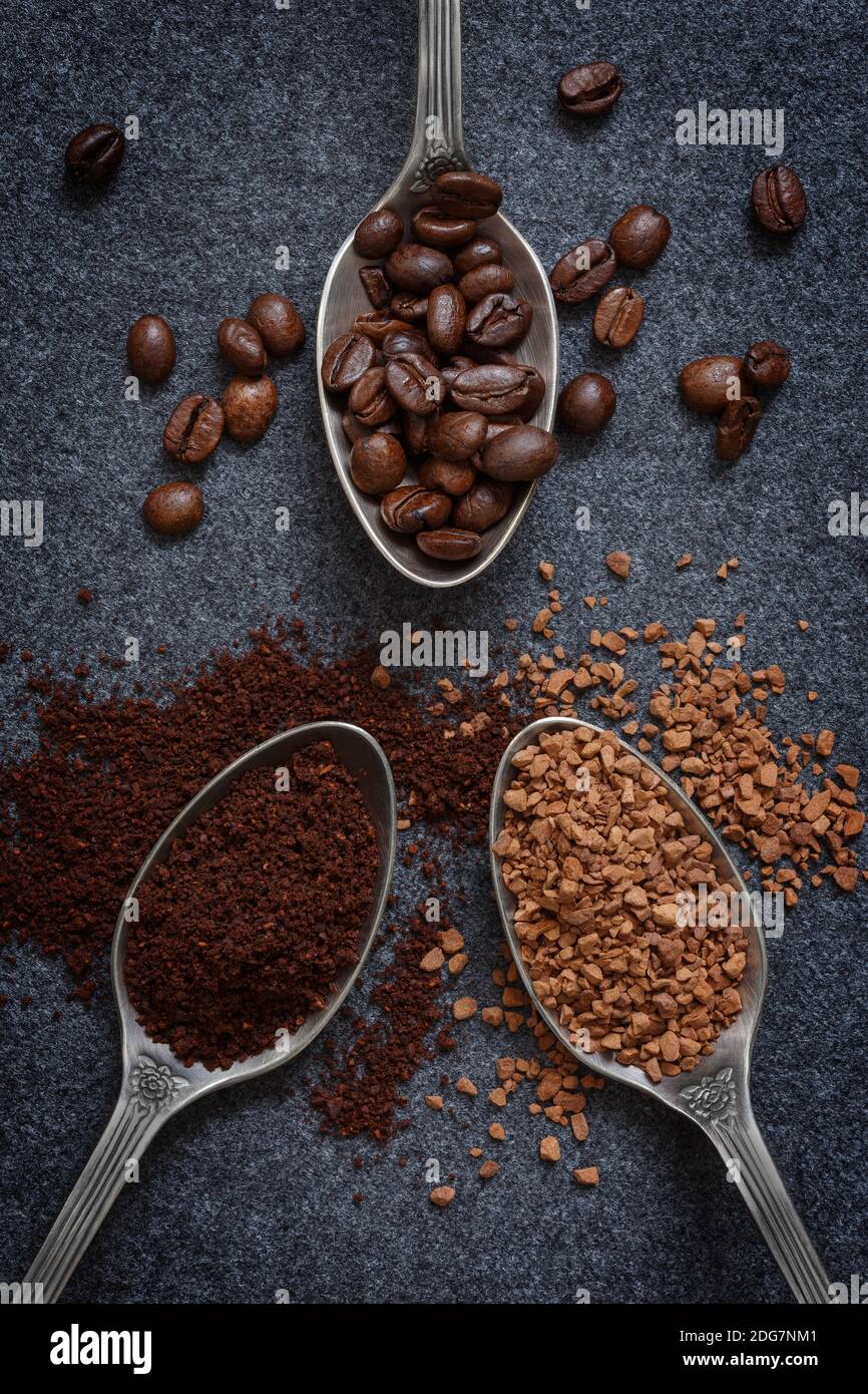 Tre cucchiai d'argento con diversi tipi di caffè: Chicchi, macinati e istantanei, su sfondo grigio Foto Stock