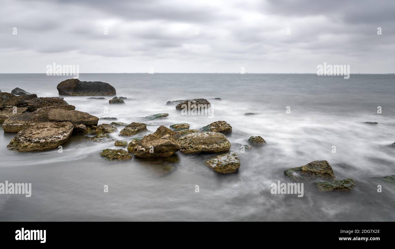 Lunga esposizione, spiaggia rocciosa di mare a tempo nuvoloso Foto Stock