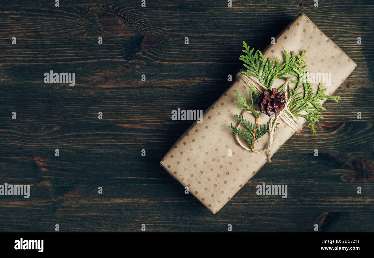 Natale zero rifiuti concetto. Accogliente confezione regalo avvolta in carta artigianale e decorata con ramificazione di cipresso verde. Sfondo di legno scuro con spazio per la copia Foto Stock