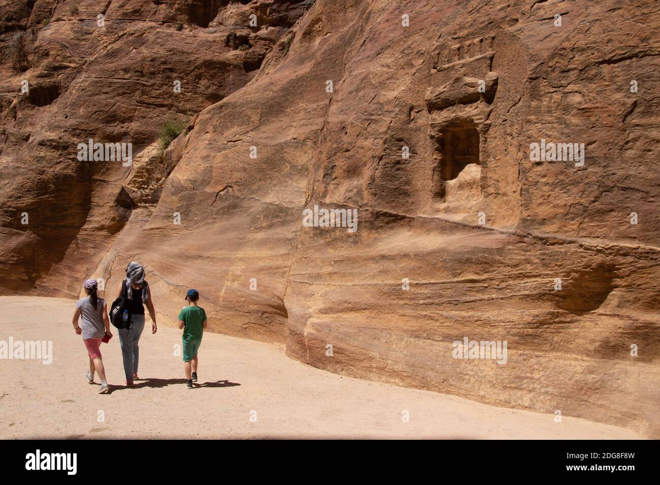 La famiglia cammina lungo il canyon dell'antica città di Petra Con sculture in pietra arenaria in giornata di sole in Giordania Foto Stock