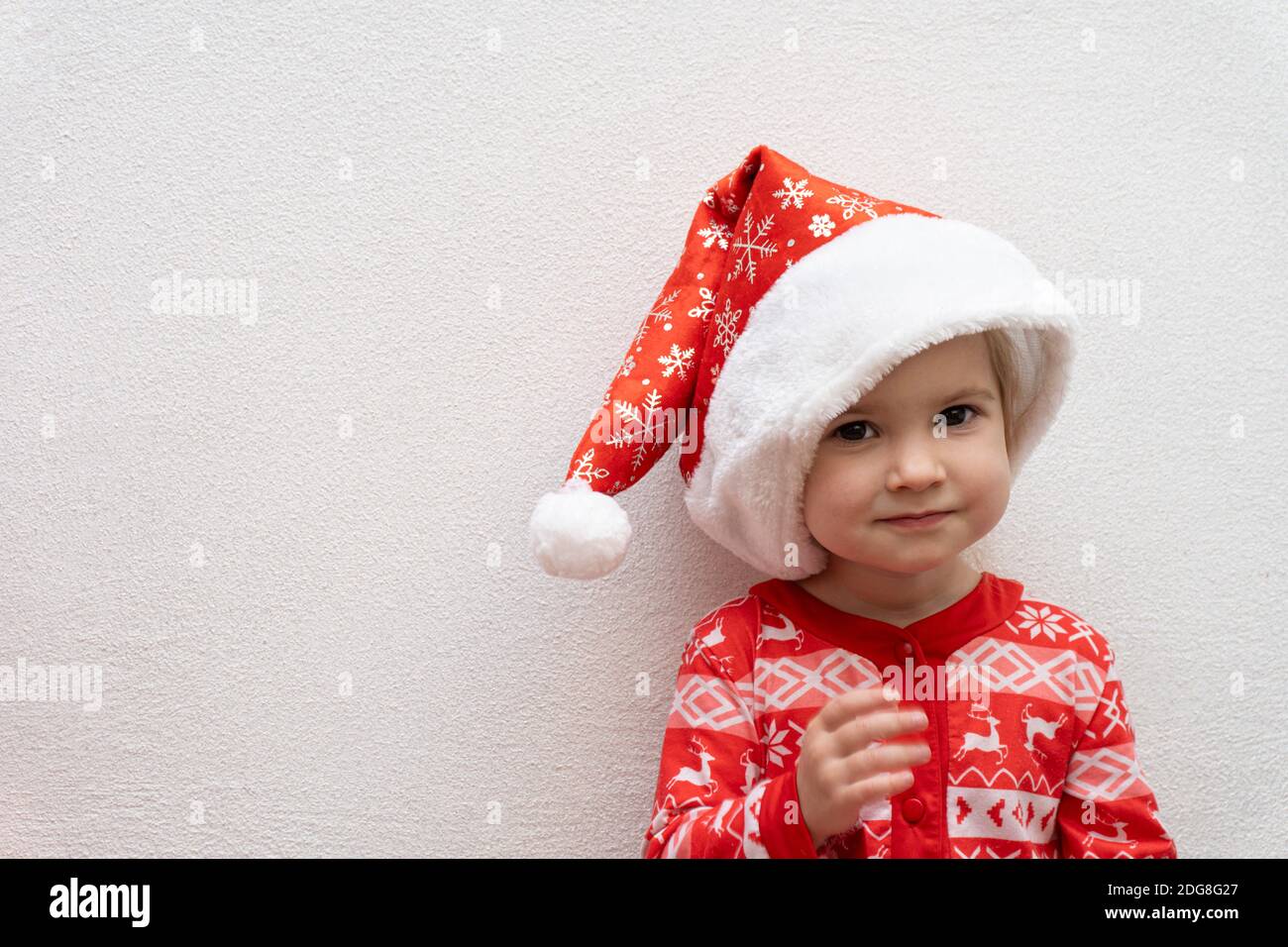 Cute bambina caucasica in rosso pigiama invernale e rosso Cappello Babbo Natale sorridente Foto Stock