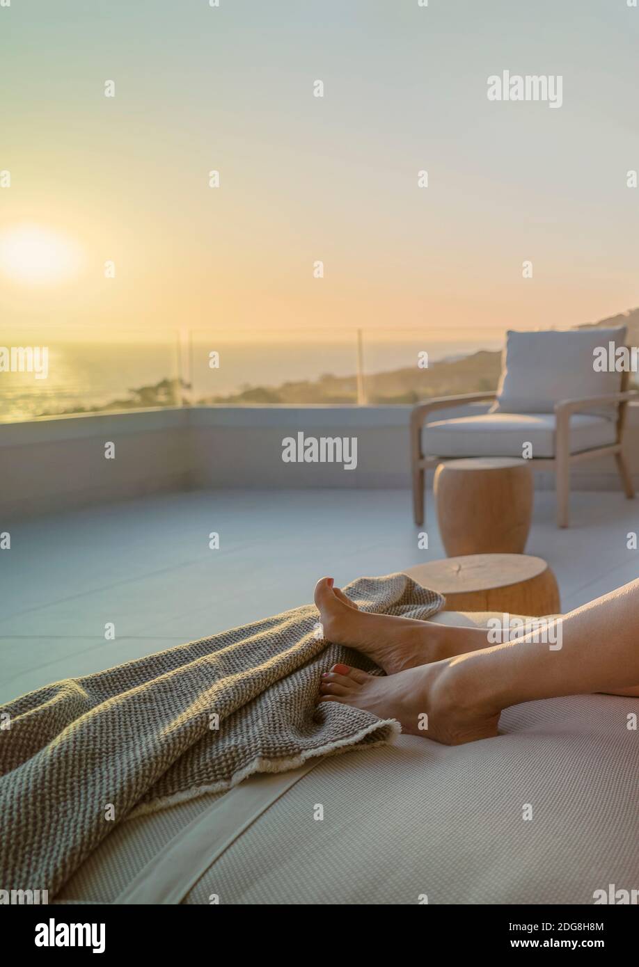 Donna a piedi nudi che gode di vista panoramica dell'oceano tramonto su un balcone di lusso Foto Stock