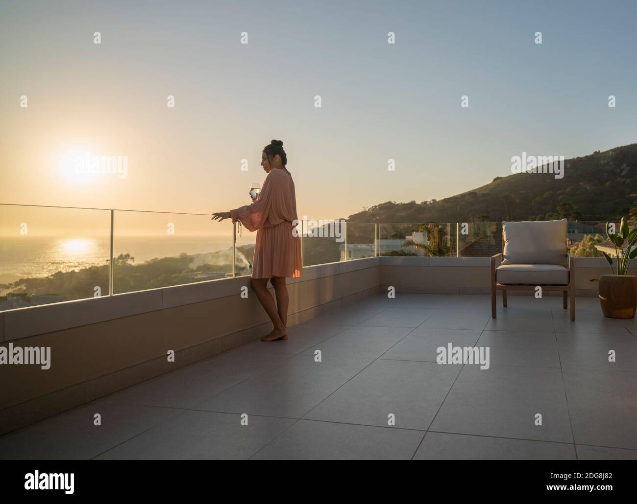 Donna che gode di vista panoramica sull'oceano al tramonto sul patio di lusso Foto Stock