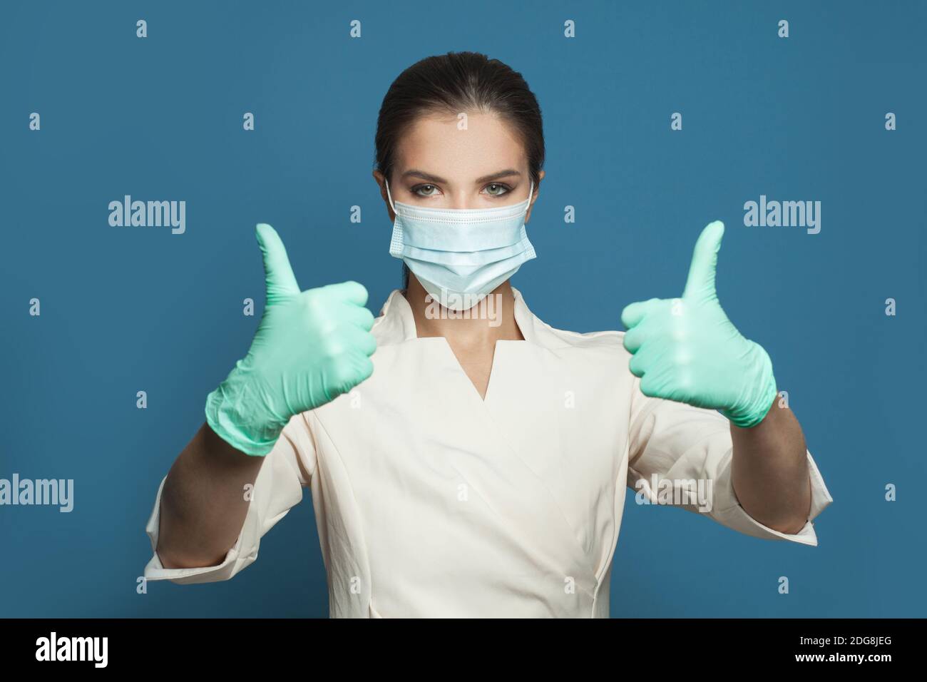 Medico in uniforme professionale e maschera protettiva che tiene il pollice su sfondo blu. Medicina, sicurezza, vaccinazione e protezione del virus covid-19 co Foto Stock