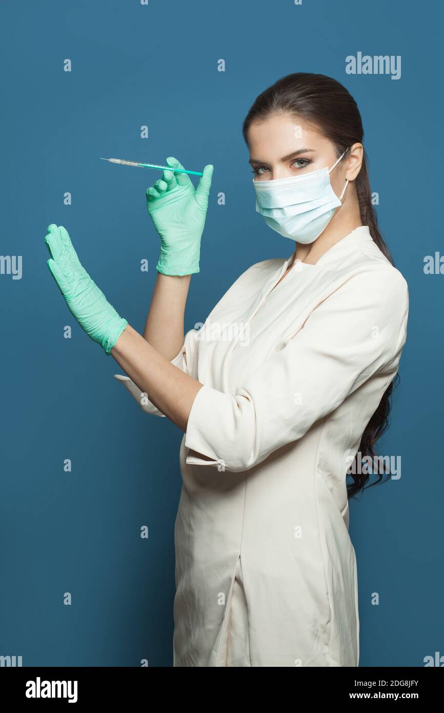 Donna medico o infermiera in uniforme medica professionale e maschera protettiva del viso con siringa su sfondo blu, medicina, sicurezza e vaccinazione co Foto Stock