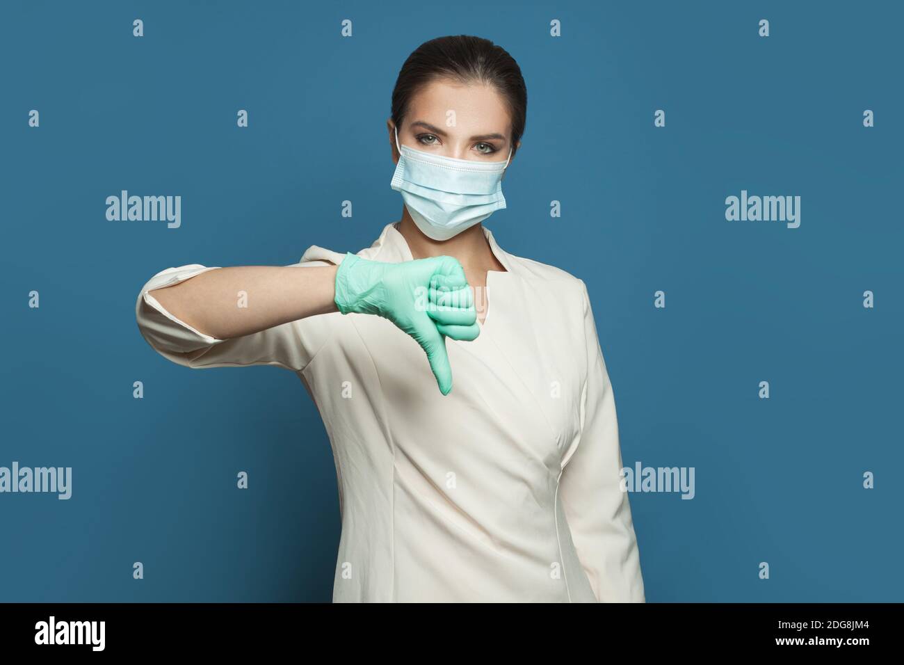 Donna medico in maschera medica protettiva mostrando il pollice giù sfondo blu Foto Stock