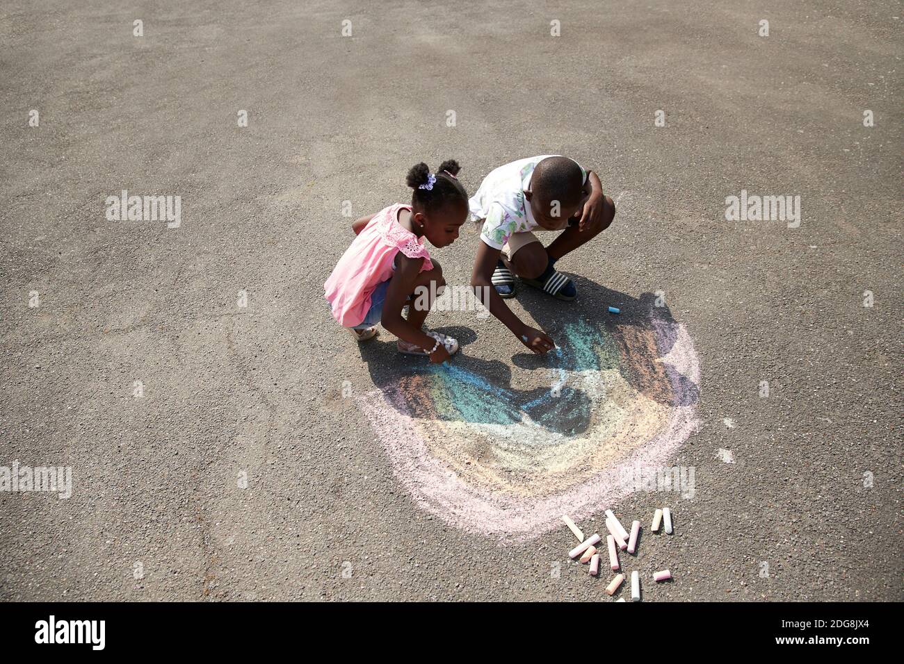 Fratello e sorella disegnano l'arcobaleno con gesso sul marciapiede Foto Stock