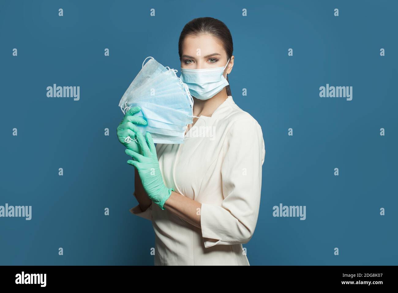 Donna medico che tiene la maschera medica protettiva su sfondo blu. Medicina, sicurezza e protezione del virus covid-19 concetto Foto Stock