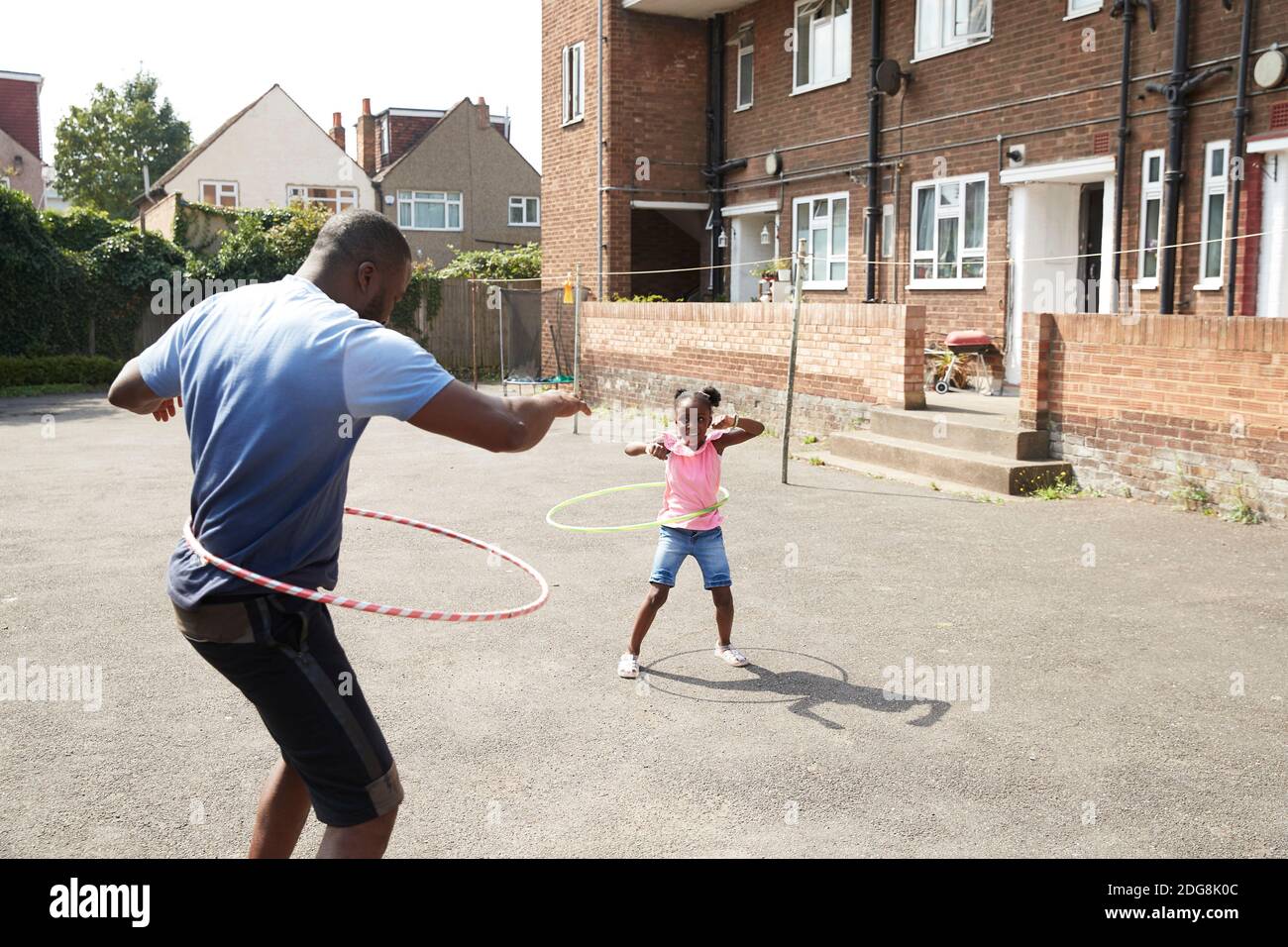 Padre e figlia giocano con cerchi di plastica in un quartiere soleggiato Foto Stock