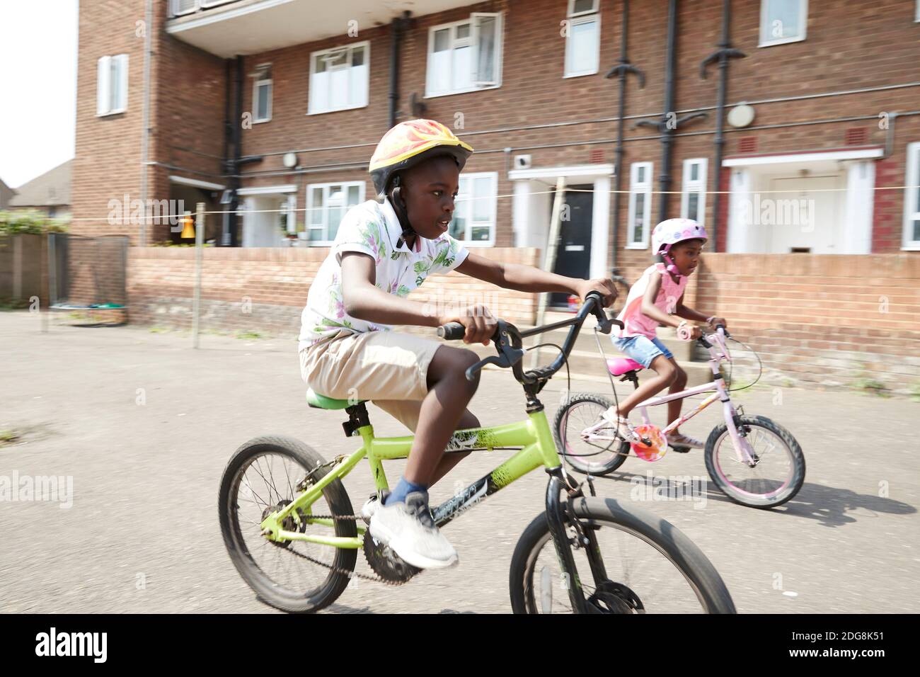 Il fratello e la sorella in bicicletta a cavallo in un quartiere soleggiato Foto Stock