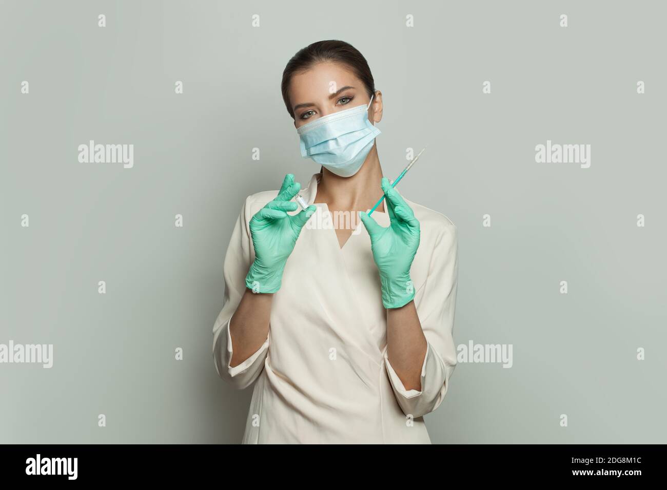 Medico o infermiere in uniforme professionale e maschera medica che contiene siringa e ampolla su sfondo bianco. Medicina, cosmetologia e vaccinazione Foto Stock