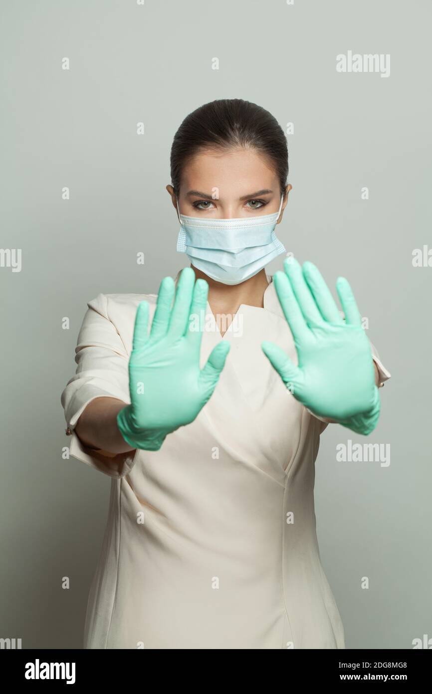 Donna medico in maschera protettiva che mostra il gesto di stop su bianco sfondo Foto Stock