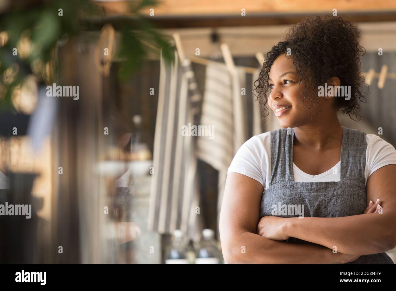 Sorridente proprietario di negozio femminile guardando via con le braccia incrociate Foto Stock