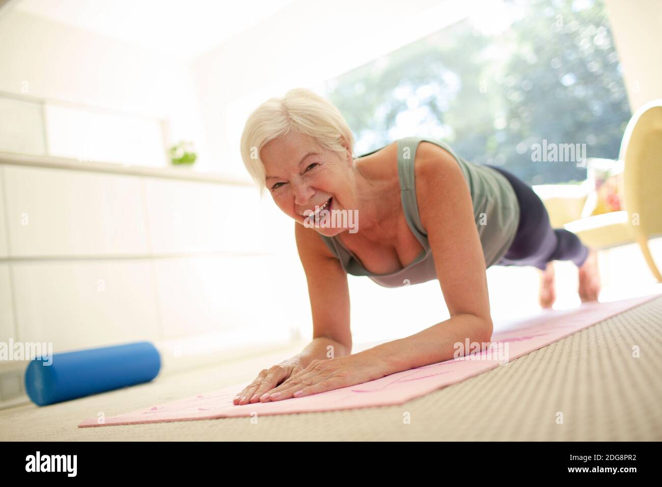 Ritratto felice donna anziana che pratica la posizione della tavola sul tappeto di yoga a casa Foto Stock