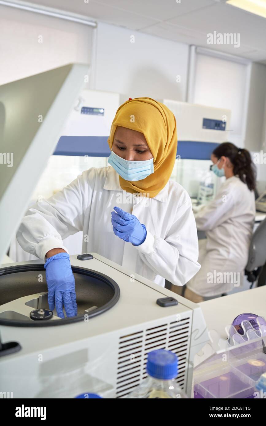 Scienziato femminile in hijab e maschera facciale con centrifuga in laboratorio Foto Stock