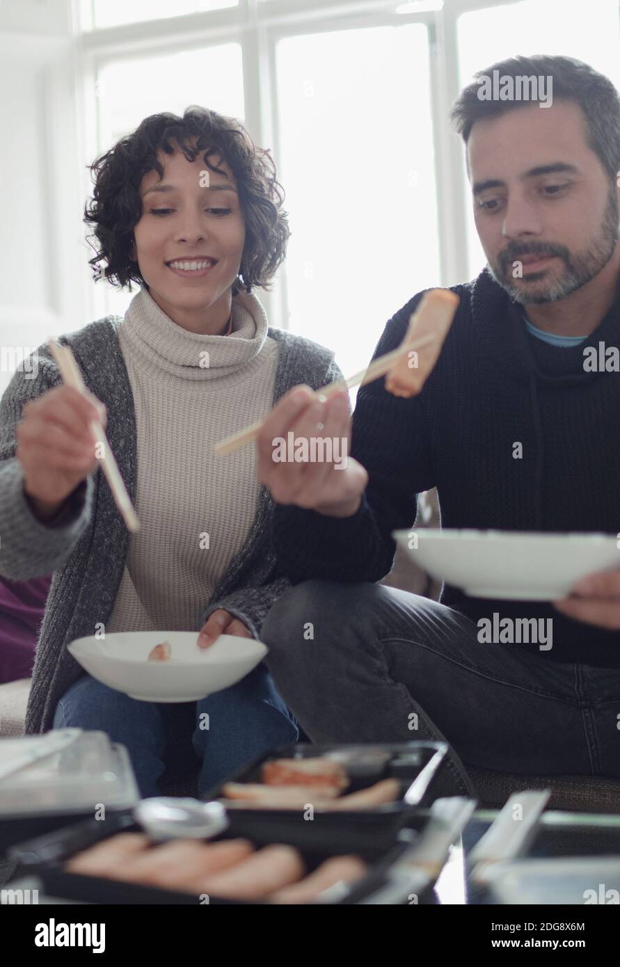Coppia gustando cibo da asporto con bastoncini nel soggiorno Foto Stock