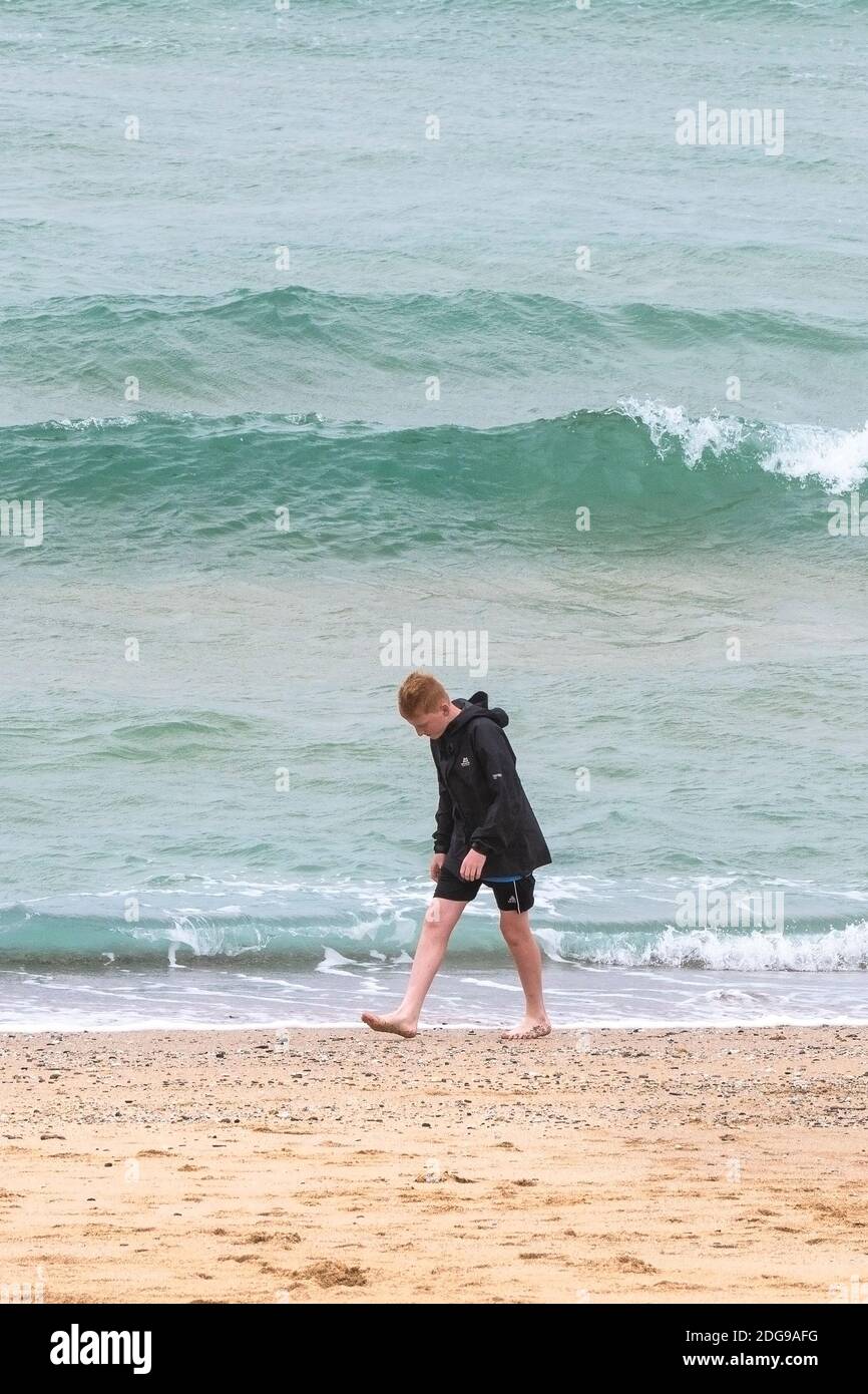 Un giovane turista maschile che cammina da solo lungo la costa di Fistral Beach a Newquay in Cornovaglia. Foto Stock