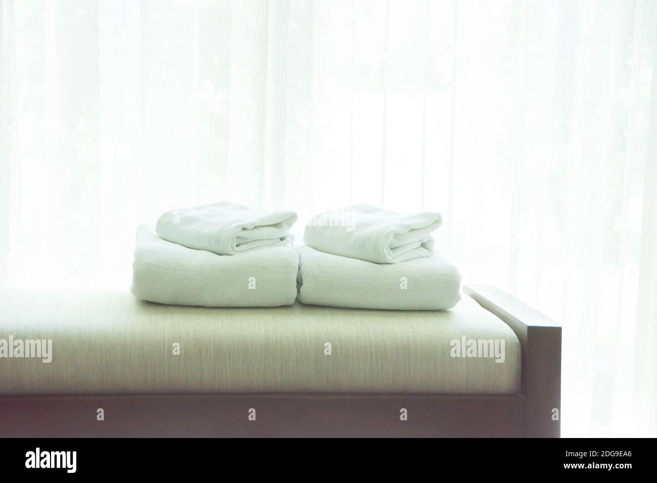 Asciugamani bianchi sono stati posati sul divano dalla finestra, con tende bianche sullo sfondo. Foto Stock