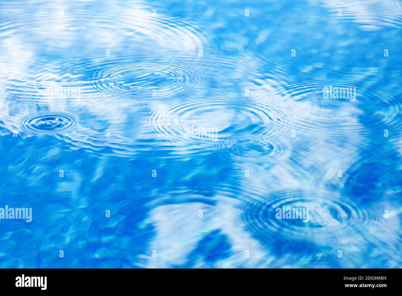 Gocce di pioggia sulla superficie blu dell'acqua della piscina. La consistenza dell'acqua blu come sfondo. Macchie circolari sull'acqua dalla pioggia Foto Stock