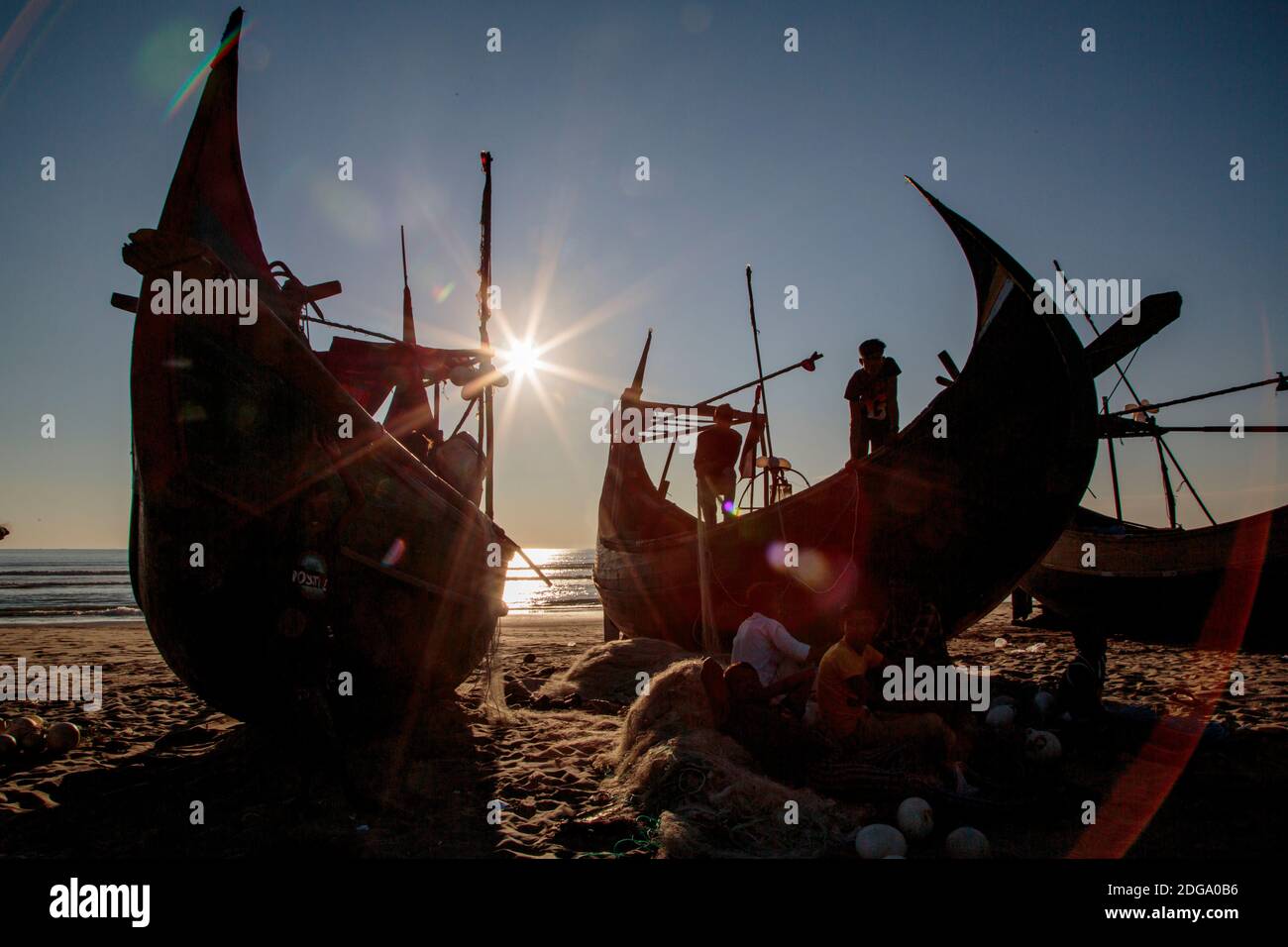 I pescatori preparano le reti da pesca prima della prossima alta marea. Le barche da pesca a forma di luna sono uniche per la zona vicino a Bazar Cox in Bangladesh. Foto Stock