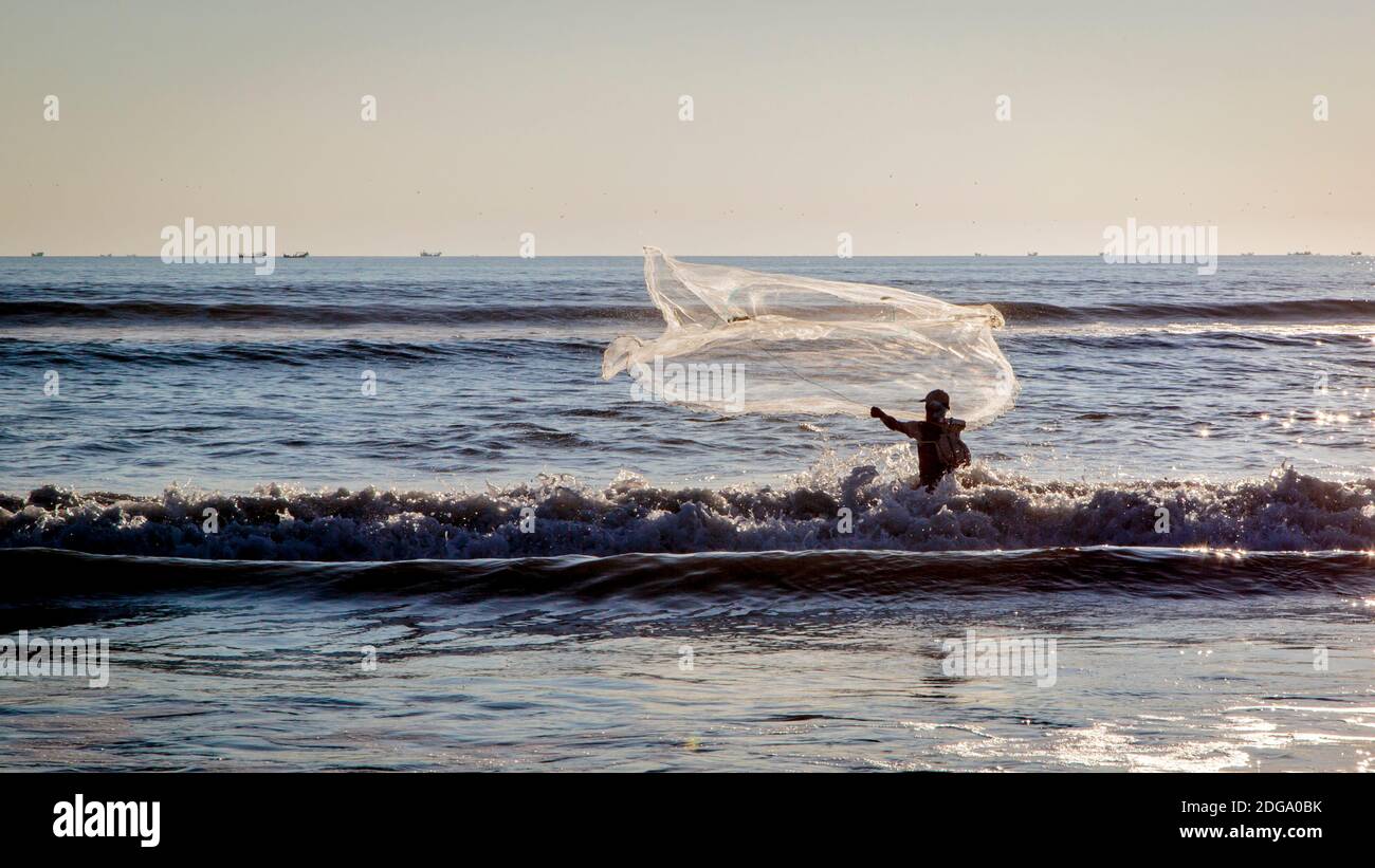 Un pescatore getta la sua rete nel surf sulla spiaggia di Cox Bazar in Bangladesh. Foto Stock