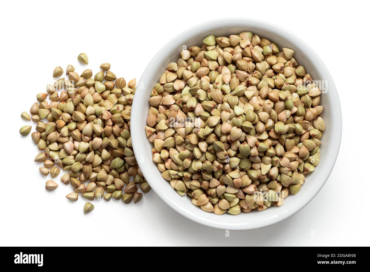 Grano saraceno verde crudo in una ciotola di ceramica bianca accanto ad un mucchio di grano saraceno verde grezzo isolato su bianco.Vista dall'alto. Foto Stock