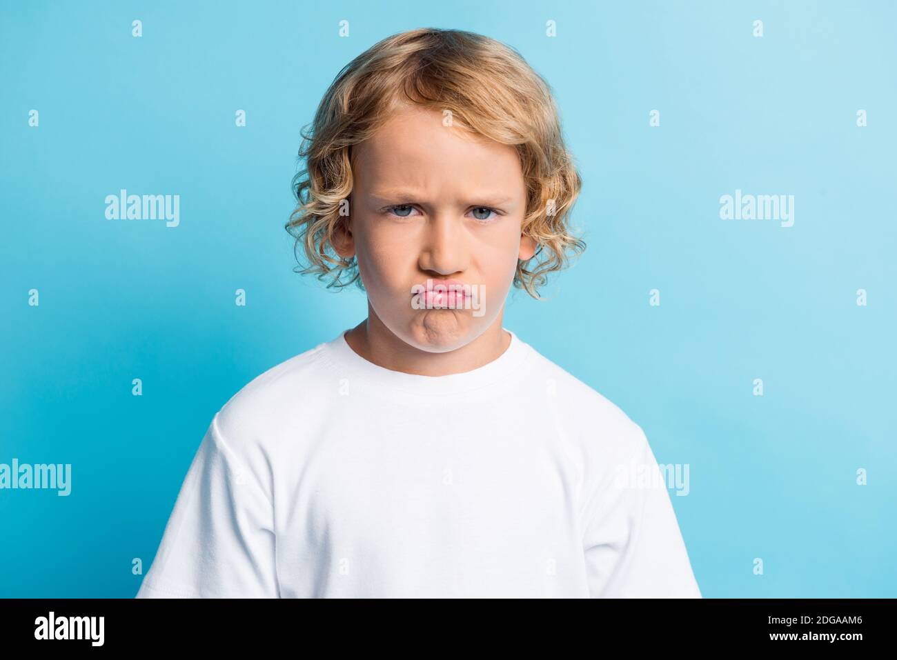 Foto di ragazzino con viso grimace che si sente deluso usura t-shirt bianca isolata su sfondo blu Foto Stock