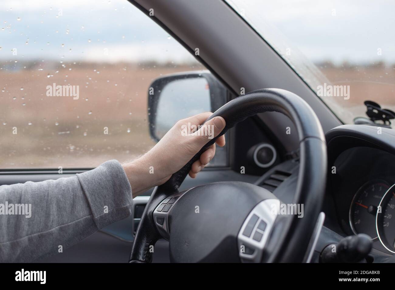 Mano maschio sul volante di una macchina Mitsubishi. Pioggia d'autunno fuori dalla finestra. Guida confortevole in SUV. Foto Stock
