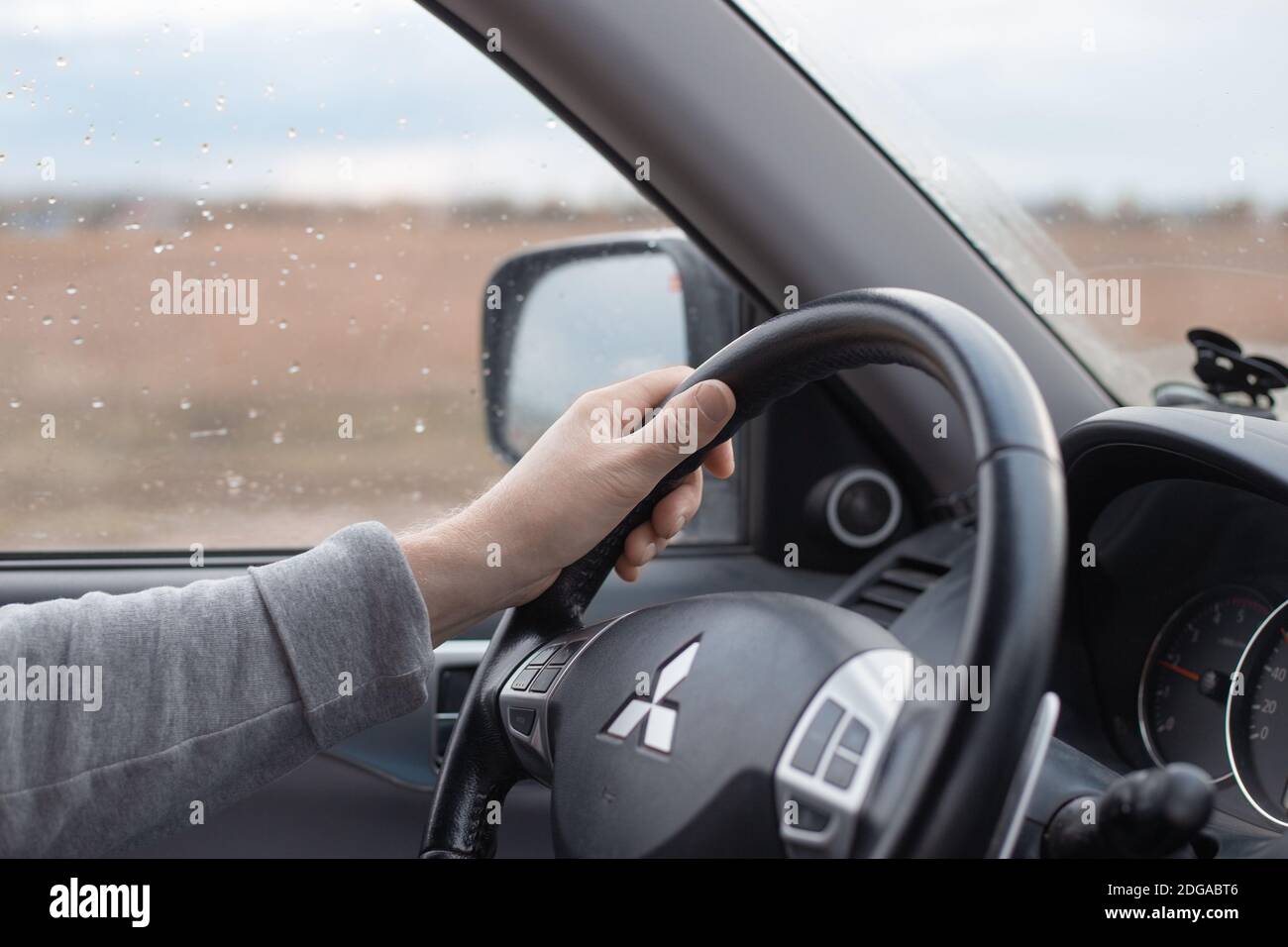 Krasnodar, Russia - 11.02.2020:mano maschile sul volante di una macchina Mitsubishi. Pioggia d'autunno fuori dalla finestra. Guida confortevole in SUV Foto Stock