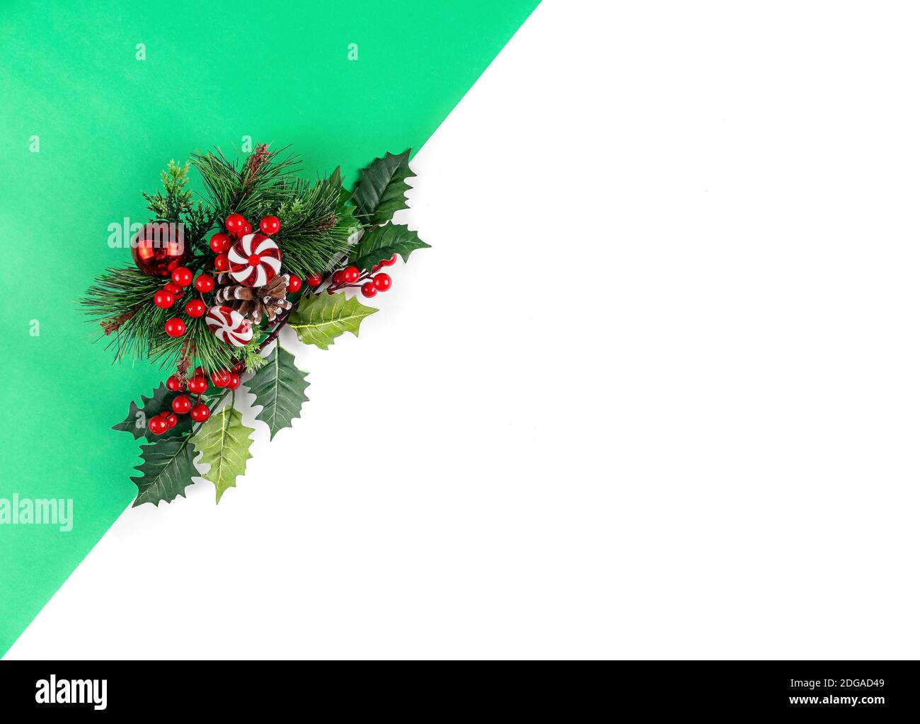 Sfondo verde e bianco. Rami realistici dell'albero di Natale con l'agrifoglio, le foglie, la palla rossa e il lollipop. Disposizione piatta. Foto Stock