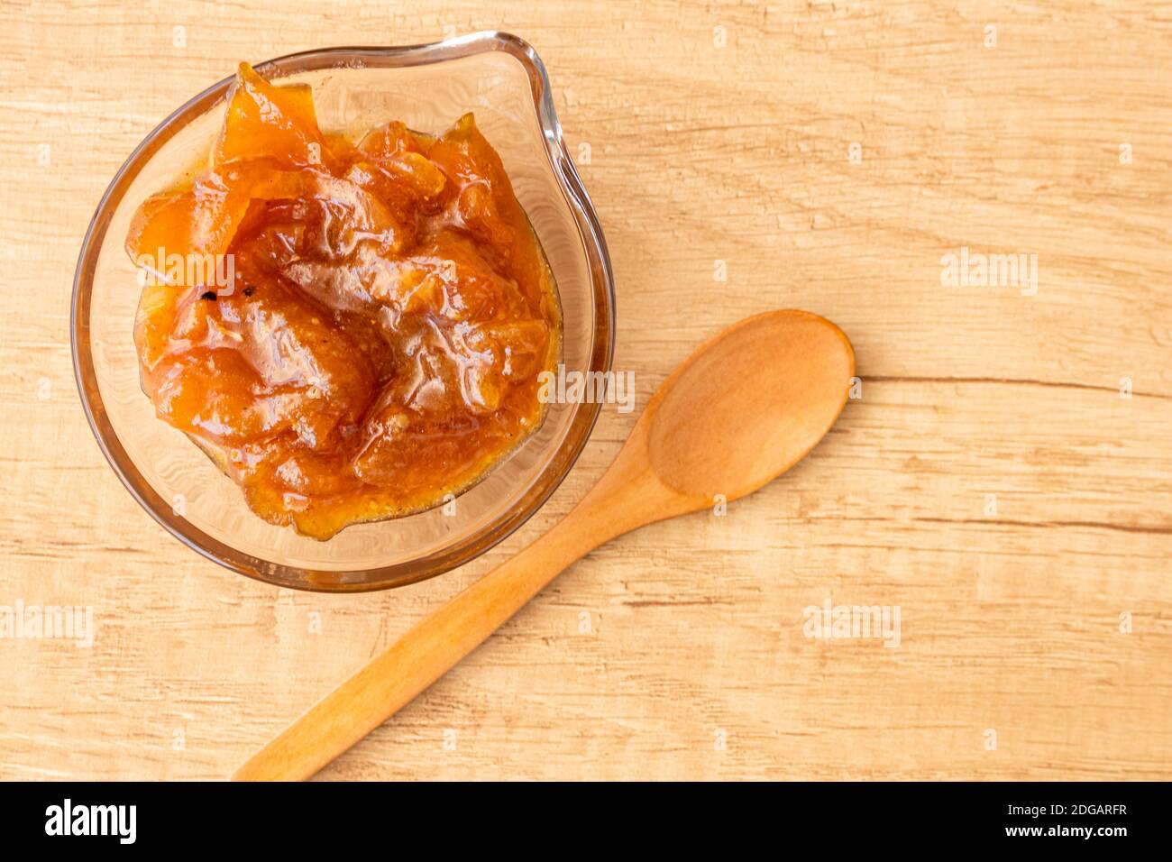 Pentola di vetro con un delizioso chutney fatto in casa di mele e cipolle, con cannella su un pannello di legno chiaro. Marmellata perfetta per la colazione. Foto Stock