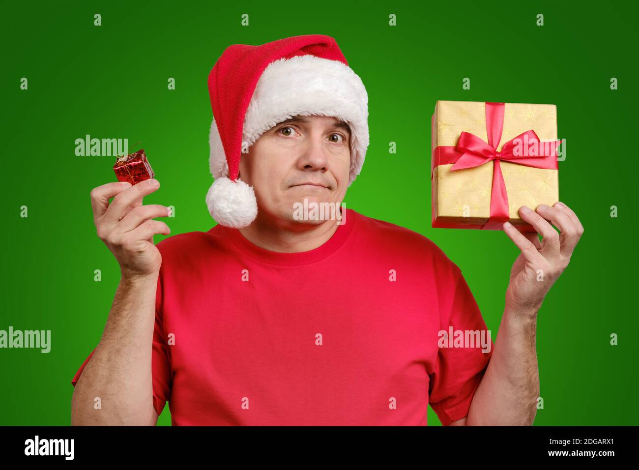 L'uomo in cappello di Santa tiene i piccoli e grandi regali di Natale su sfondo verde Foto Stock
