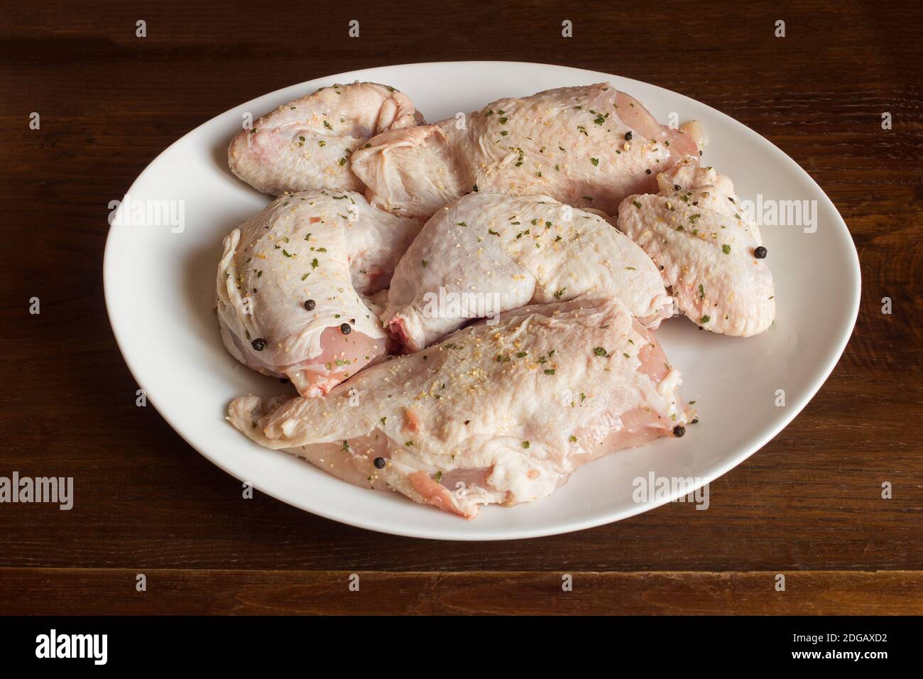 Un piatto con un pollo intero crudo disossato condito con sale, pepe nero e spezie. Cibo e carne. Fondo di tessitura organico. Foto Stock