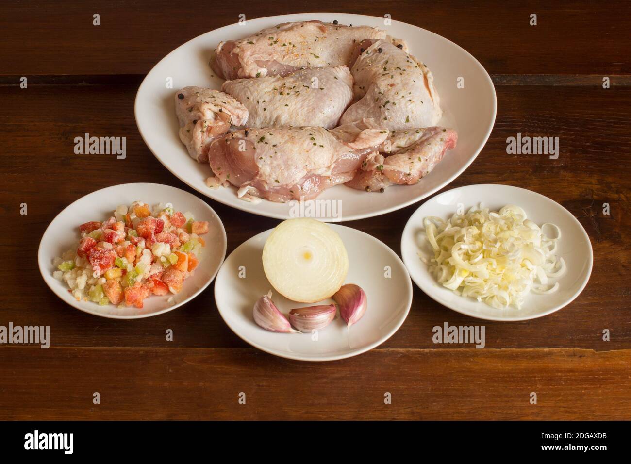 Presentazione degli ingredienti crudi per la preparazione della ricetta di pollo in salsa vegetale su fondo rustico di castagno. Carne e verdure. Foto Stock