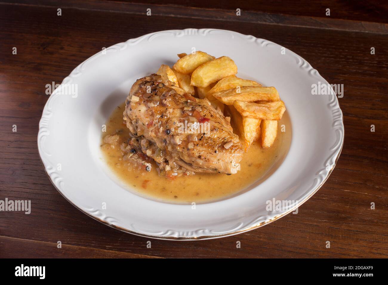 Presentazione di un pasto di pollo con salsa vegetale e patate su un piatto di porcellana bianca. Ricette della cucina. Foto Stock