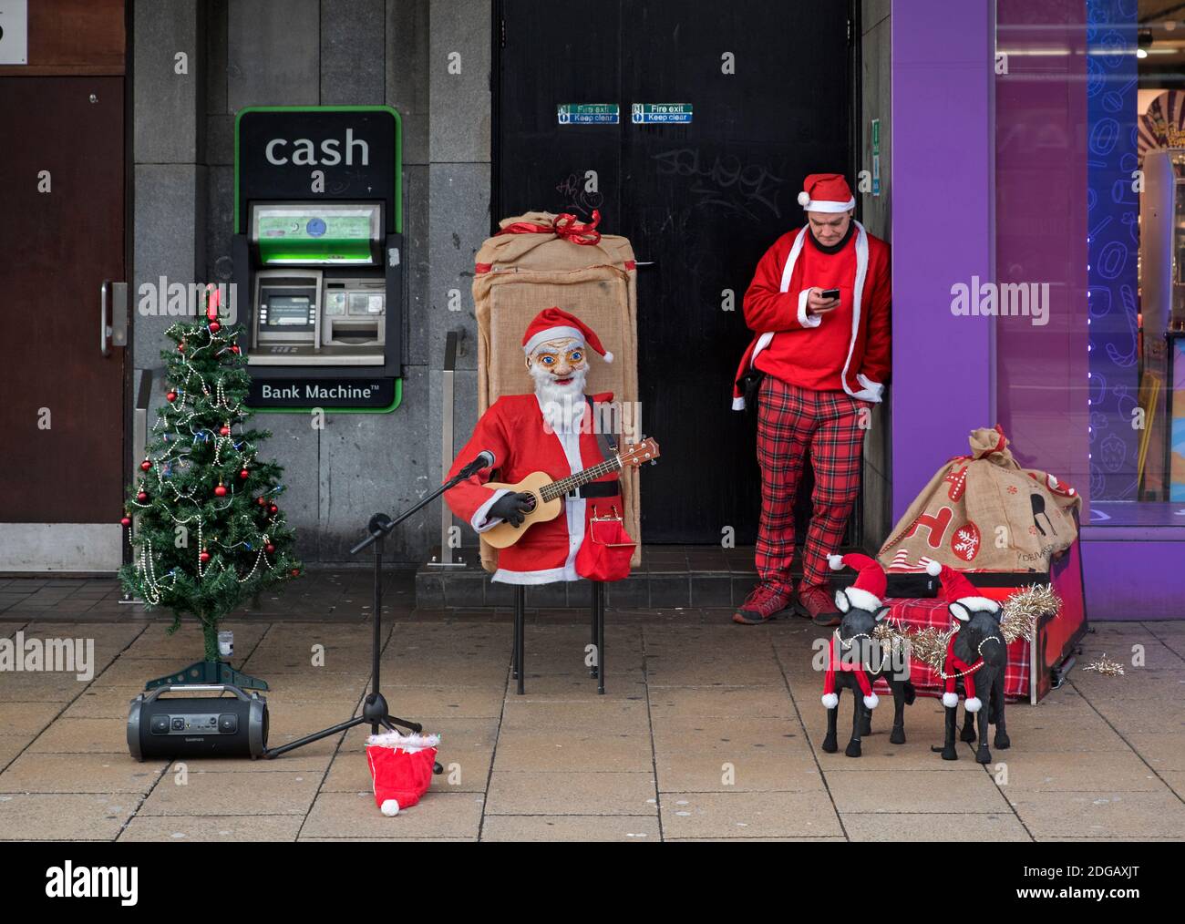 Busker vestito in costume di Santa ha una pausa e controlla il suo telefono su Princes Street, Edimburgo, Scozia, Regno Unito. Foto Stock