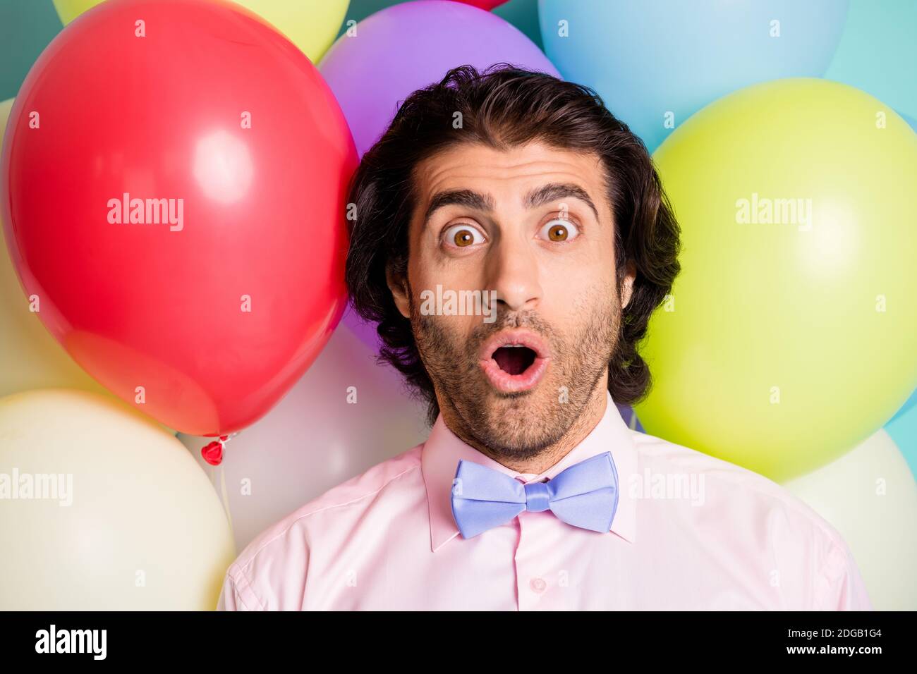Ritratto di gentiluomo sorpreso a bocca aperta camicia rosa prua viola su sfondo luminoso molti palloncini creativi Foto Stock