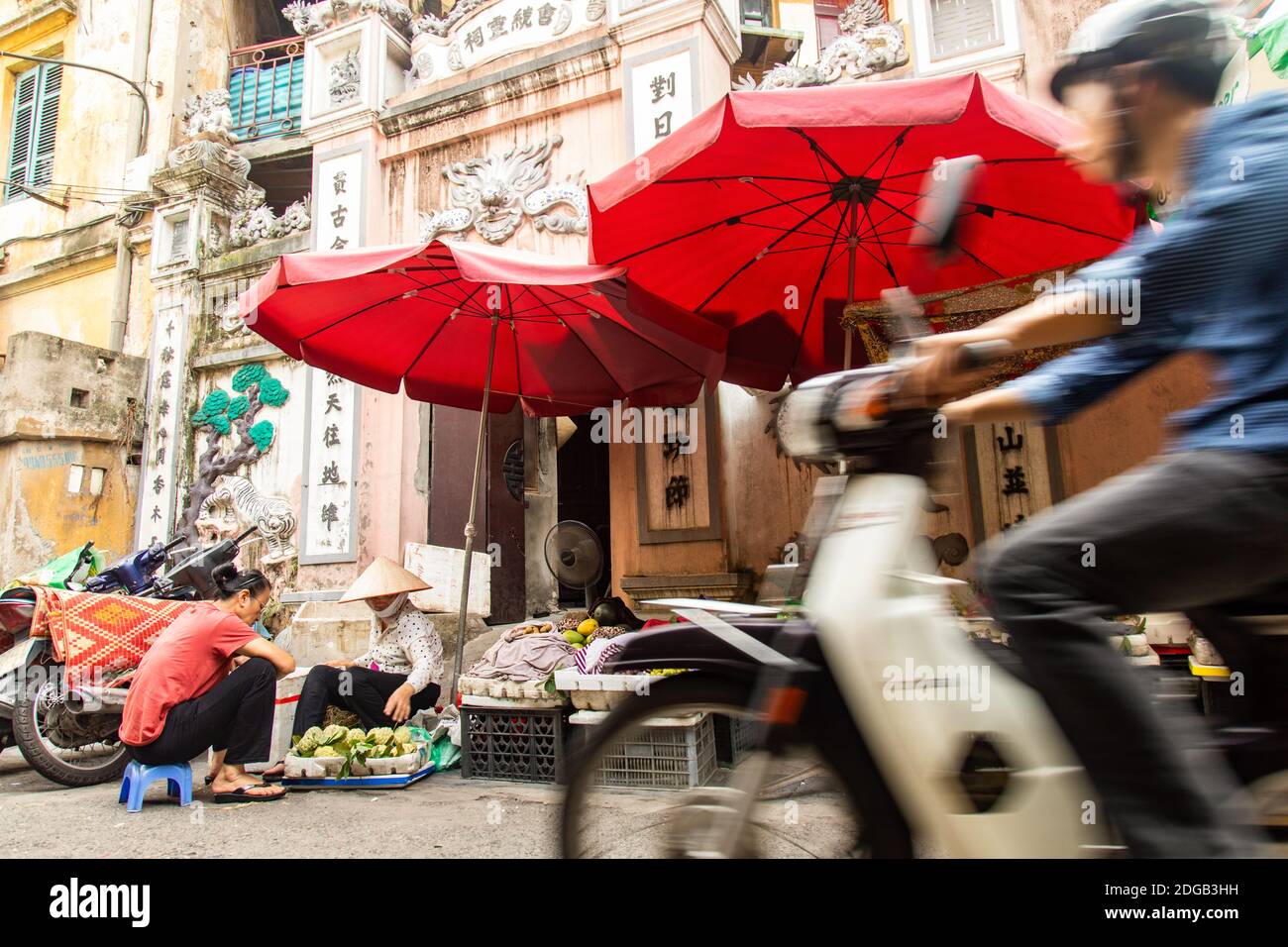 Venditori vietnamiti nella caotica città di Hanoi, dove i mercati di strada si trovano tra moto e veicoli Foto Stock