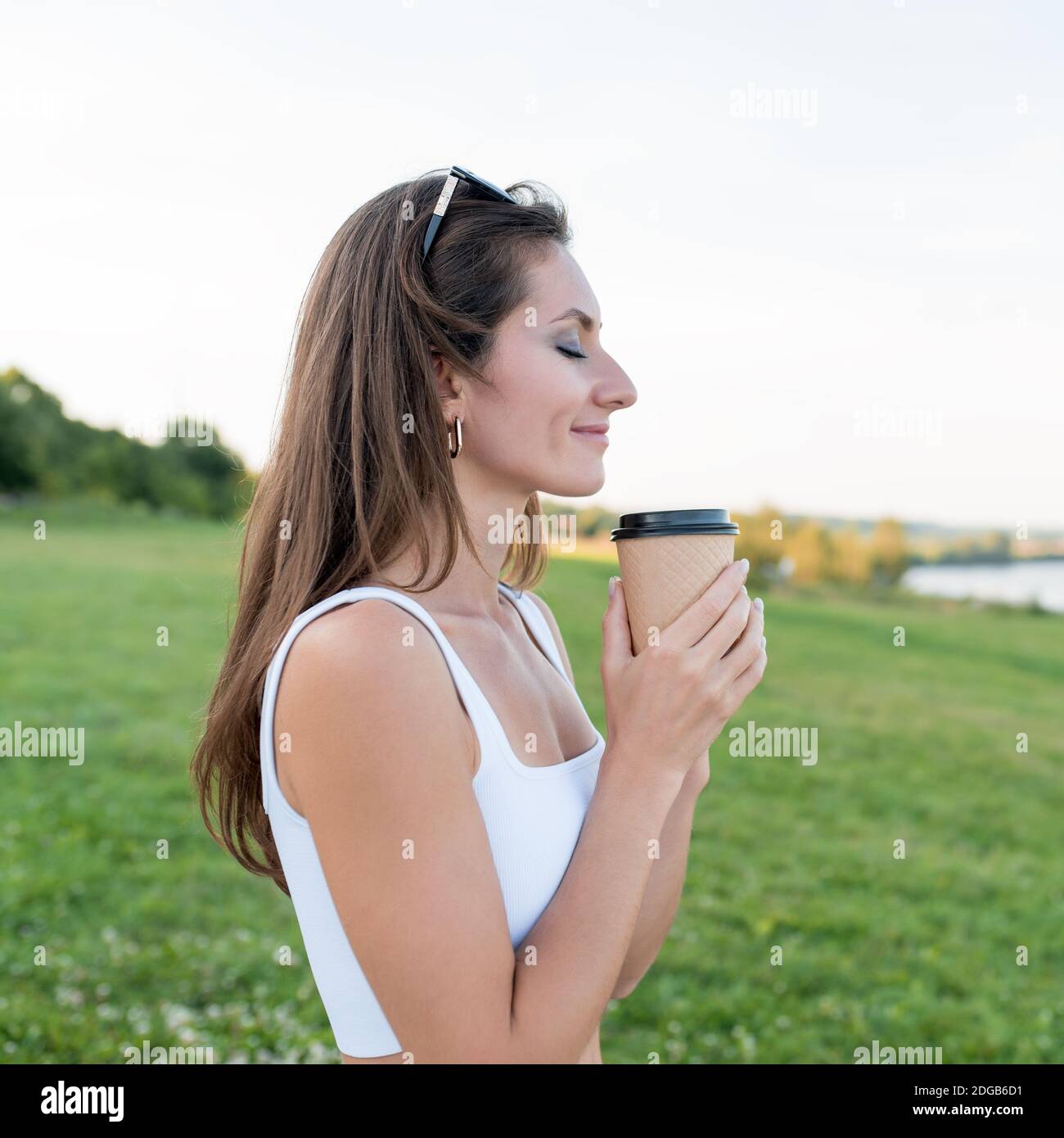 Donna felice che tiene la tazza con il tè del caffè nelle sue mani, emozioni di felicità, godimento e relax nel fine settimana. Estate nel parco in natura tema bianco Foto Stock