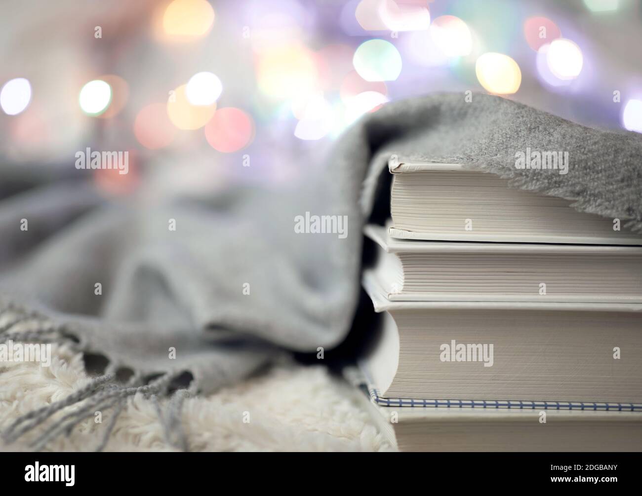 Una calda coperta di lana lavorata a maglia, luci colorate per l'arredamento della casa e un mucchio di libri sul letto. Tempo di leggere a casa. Atmosfera accogliente e confortevole Foto Stock